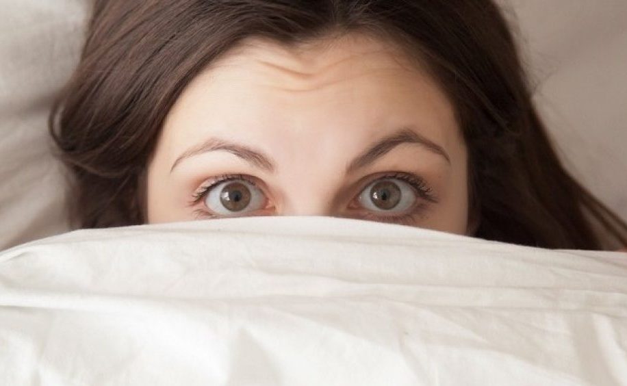 Funny surprised girl covering face with white blanket, headshot closeup Funny surprised girl covering half of face with white blanket, young scared woman hiding and peeking from duvet, afraid of night monsters, feels embarrassed, wide awake, head shot close up, top view